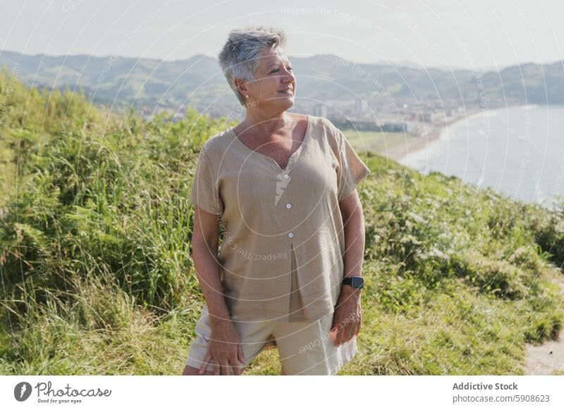 Senior woman enjoying scenic coastal view senior mature elderly contemplative field lush outdoor leisure relaxation serene peaceful nature landscape