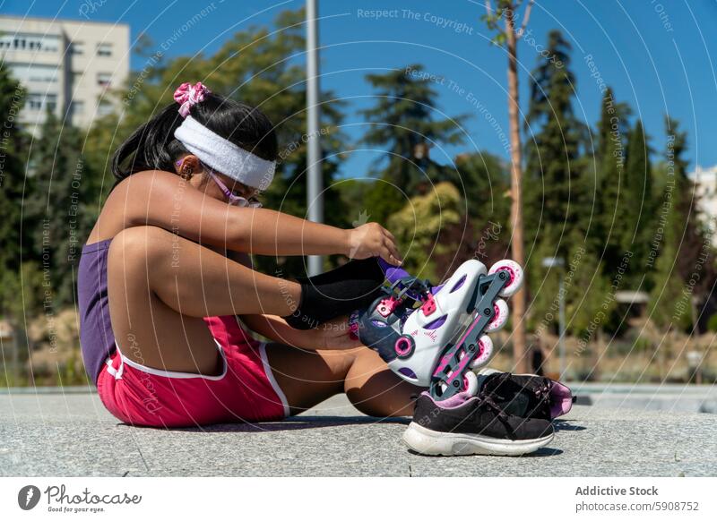 Young girl putting on rollerblades in a sunny park tree pavement concentrate strap skate fun day skating colorful outdoor activity sport rollerblading child