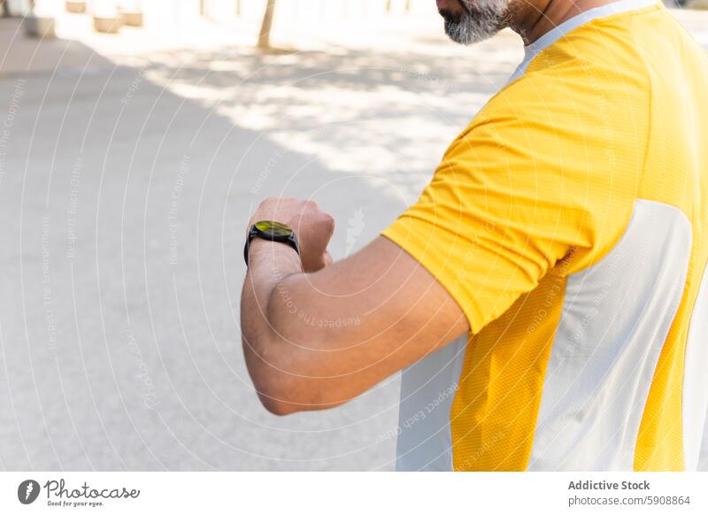 Man checking smartwatch during outdoor workout session man time fitness technology sport gadget device summer yellow shirt wrist digital monitor health exercise