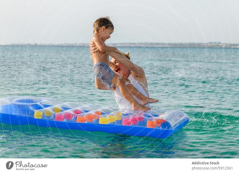 Joyful mother and son playing on a floating in the sea beach italian fun summer joy water holiday vacation family child parent mat outdoor daytime clear blue