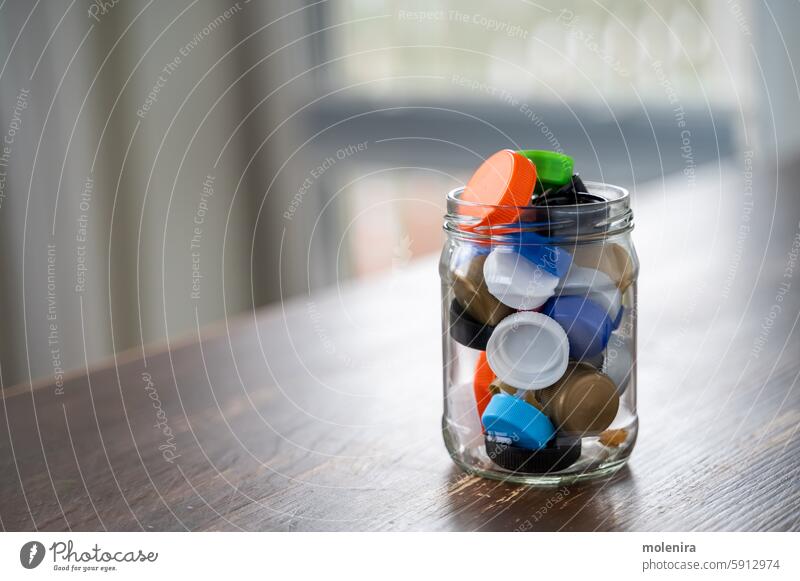 Glass jar filled with colorful plastic bottle caps recycling reuse environmental sustainability eco-friendly glass wooden table collecting full transparent