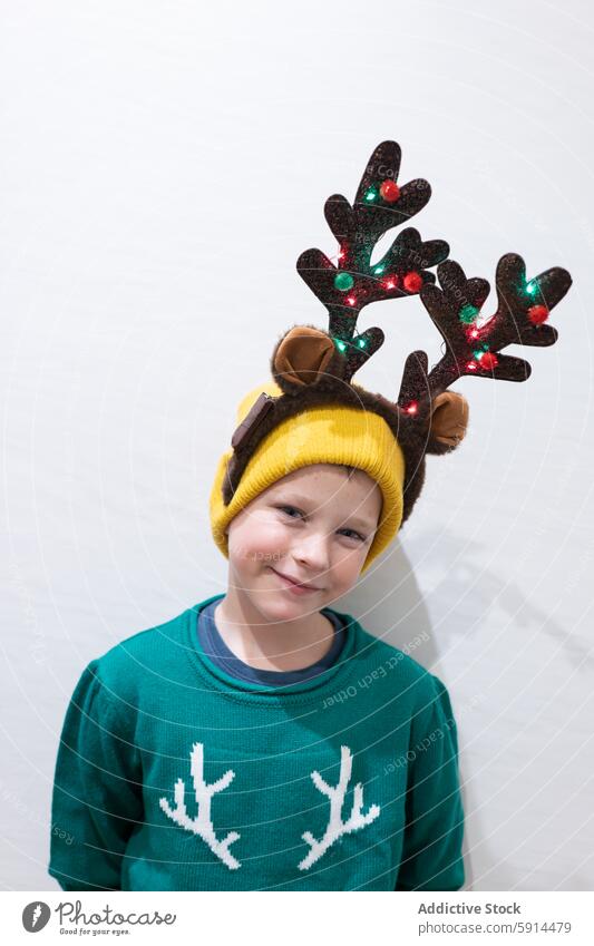 Young boy wearing festive reindeer antlers christmas sweater green smile cheerful holiday decoration glowing light child joy celebration warmth december happy