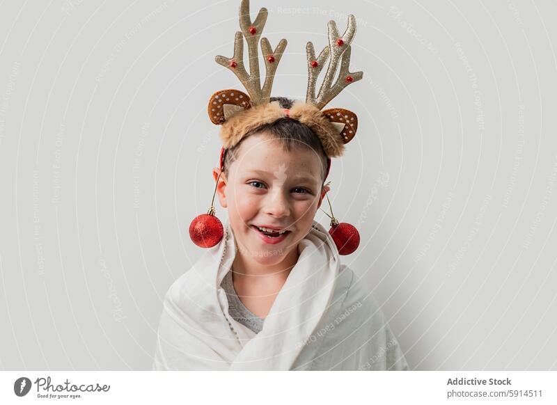 Cheerful boy in reindeer headband with Christmas ornaments christmas red bauble smile festive spirit holiday decoration cheerful joy fun child youth costume