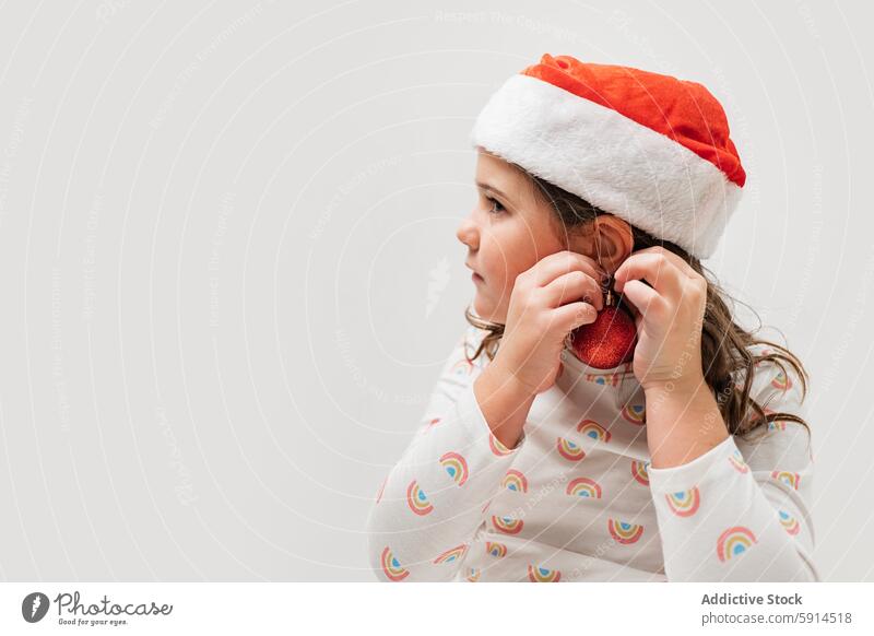 Young girl in Santa hat holding a Christmas ornament christmas santa hat red holiday winter celebration decoration cheerful festive child female joy season