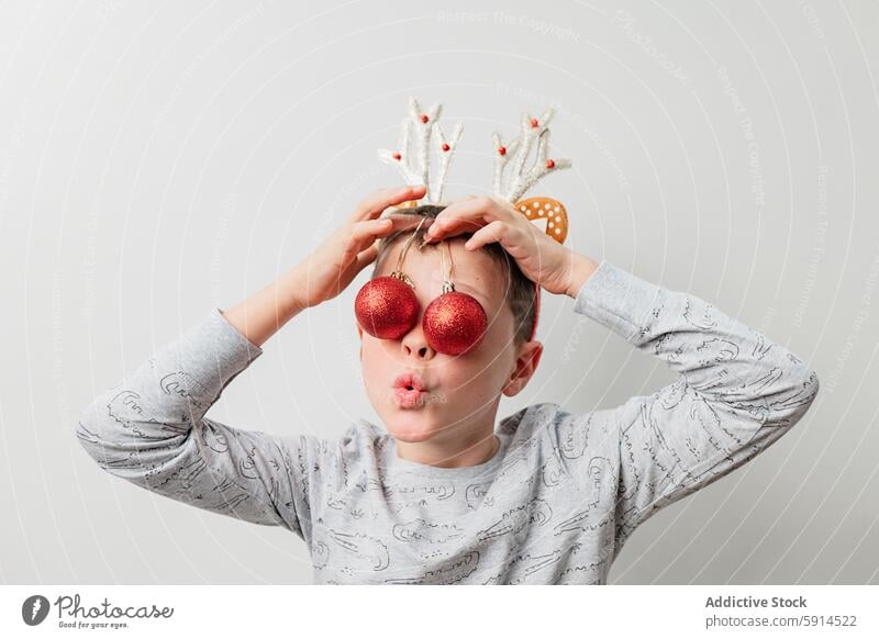 Playful boy with reindeer antlers and Christmas baubles christmas playful holiday decoration festive fun child humor red white gray shirt funny face joy