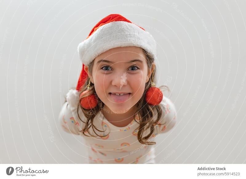 Young girl celebrating Christmas with festive cheer christmas santa hat smile holiday cheerful young child tongue earring red ball decoration joy spirit