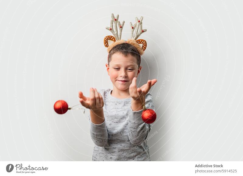 A young man with a reindeer headband playing with Christmas decorations christmas boy ornament festive toss joy spirit background red light-gray celebrate