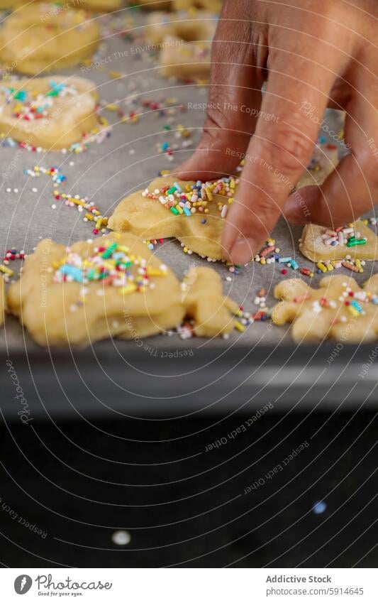 Adding sprinkles to animal-shaped sugar cookies hand decoration baking sheet colorful close-up kitchen homemade pastry dough cooking activity family sweetness