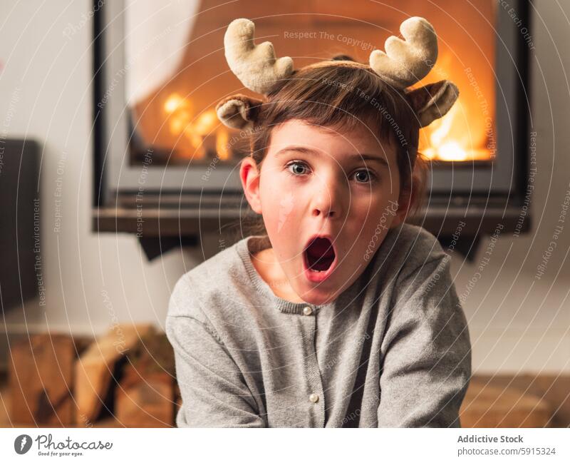 Young girl with reindeer antlers celebrates Christmas child christmas excitement surprise cozy room fireplace celebration festive holiday winter joy expression