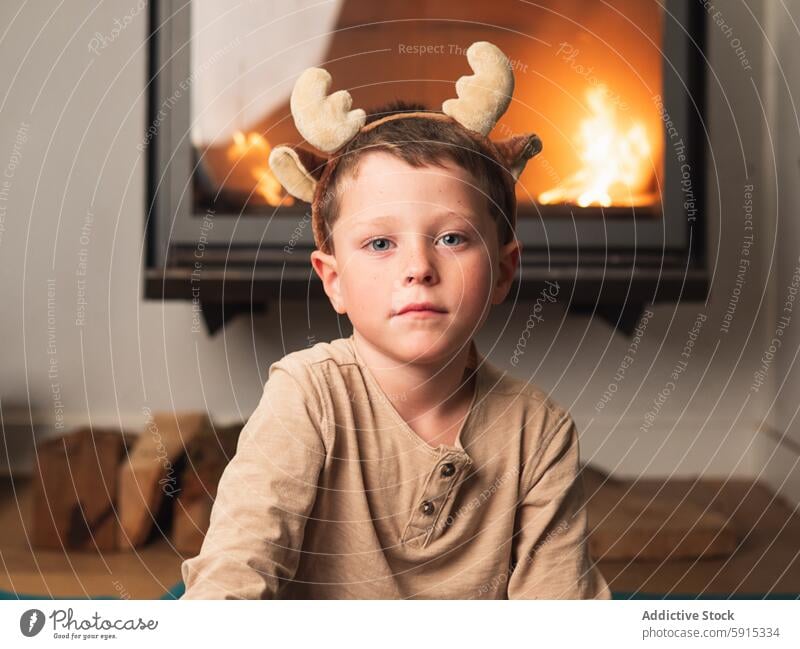 Young boy wearing reindeer antlers by a fireplace child christmas warmth cozy festive solemn indoor celebration holiday seasonal decoration winter eve young