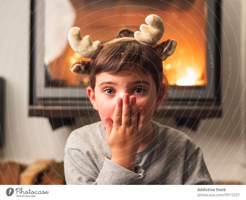 Little girl with reindeer antlers celebrating Christmas child christmas celebration surprise fireplace cozy festive home joy young holiday winter season warmth