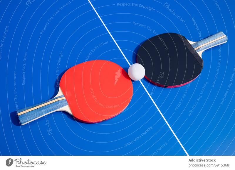 Table tennis paddles and ball on a blue table sport game ping pong red black equipment competition play leisure activity exercise match racquet plastic simple