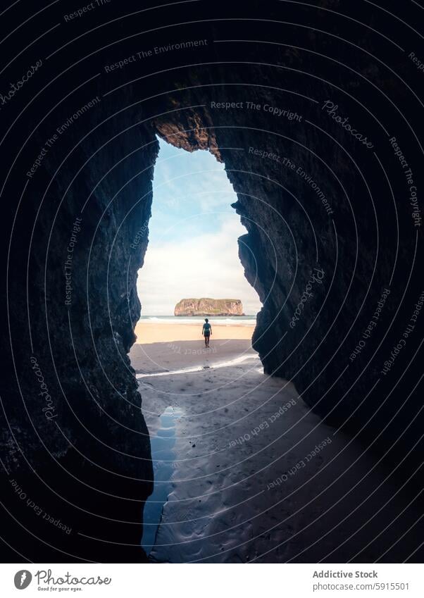 Explorer on the sandy shores between rocky cliffs at Asturias llanes asturias explorer beach arch silhouette sunlight water dramatic serene playa de andrin cave