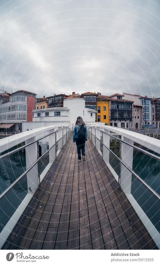 Woman walking on bridge with colorful buildings in Llanes woman llanes asturias travel tourism architecture urban sky moody wanderlust stroll modern serenity