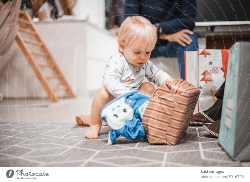 Cute little blond Caucasian toddler unpacking Christmas or Birthday present. Adorable small infant baby boy opening gift child celebration birthday room