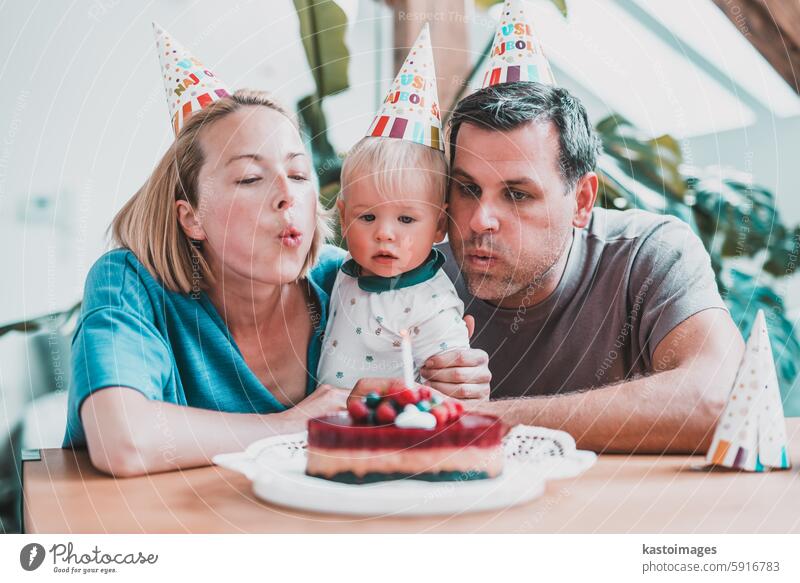 Happy little boy son going to blow candles on cake while celebrating Birthday with young loving parents, excited kid raising arms and smiling while receiving congratulations and presents from family