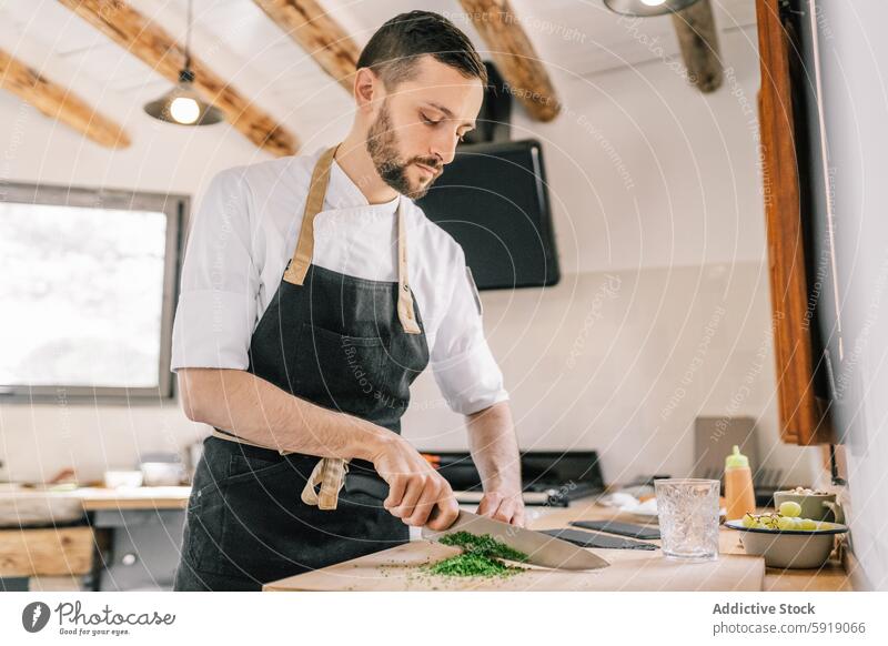 Private chef preparing meal in home kitchen cooking herbs chopping man apron focused looking down culinary professional food preparation white shirt