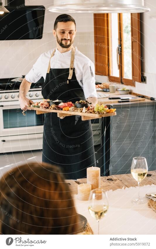 Private chef serving gourmet meal to friends in kitchen dining unrecognizable anonymous charcuterie platter board cheese fruit wine glass wood table dinner