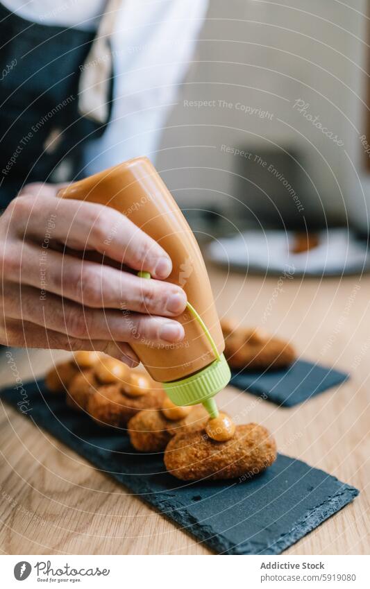 Adding sauce to crispy croquette on slate coasters kitchen cooking garnish unrecognizable anonymous faceless crop hands food preparation wooden table squeeze