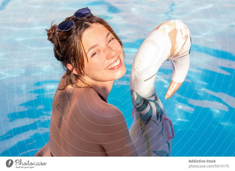 Young woman smiling in a pool with inflatable smile sunny float joy happiness summer water leisure fun relaxation tattoo swim outdoors bright sunlight cheerful