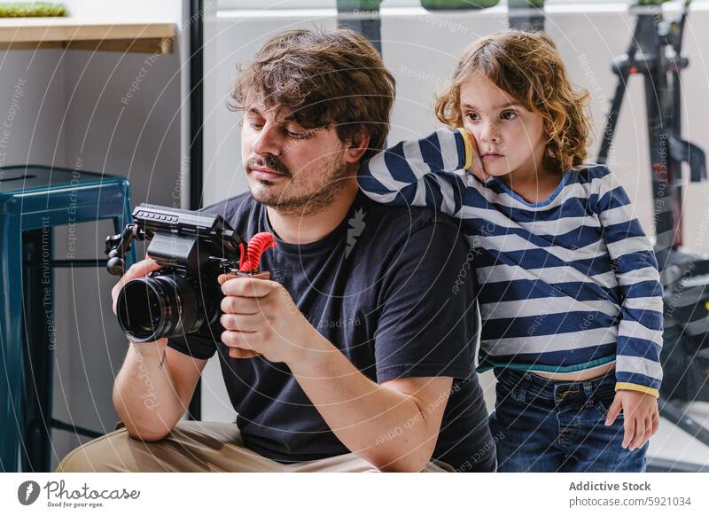 Young filmmaker with a child assistant checking equipment camera curiosity studio video review footage male leaning shoulder adult young home curious creative