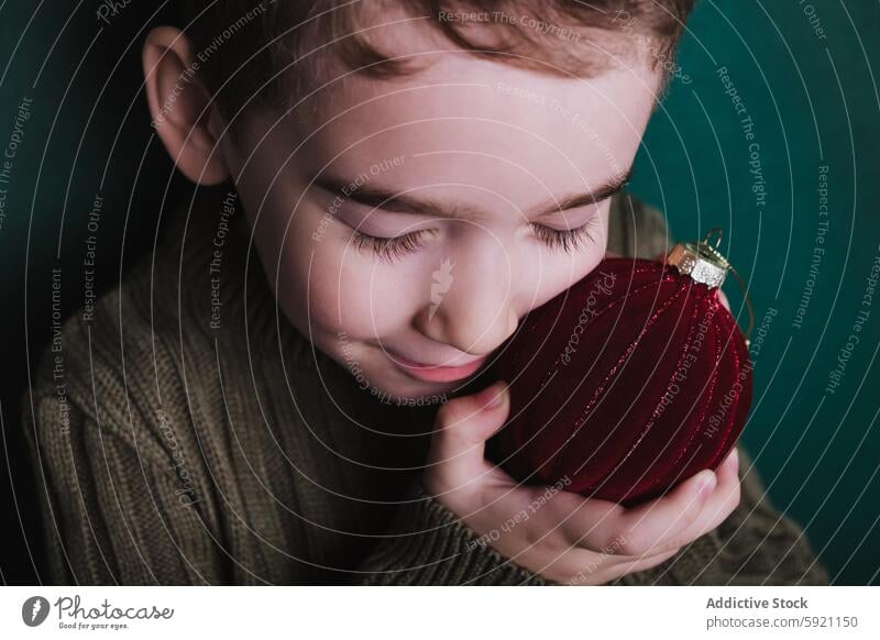 Child softly holding a red Christmas ornament child christmas holiday warmth boy velvet gentle serene closed eyes embrace festive decoration winter comfort