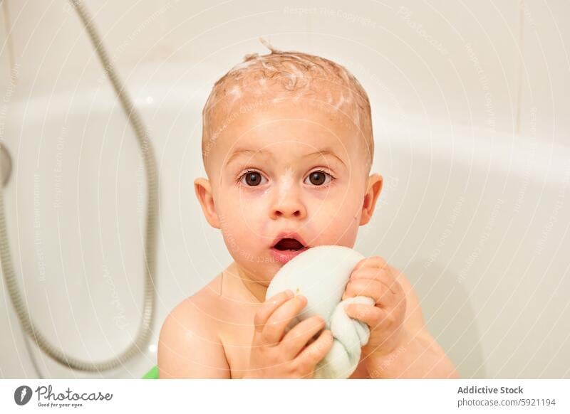 A child in the bathtub with a head full of soap and a wet towel in his hands adorable baby bathing bathroom body boy brown bubble care caucasian clean cleaning