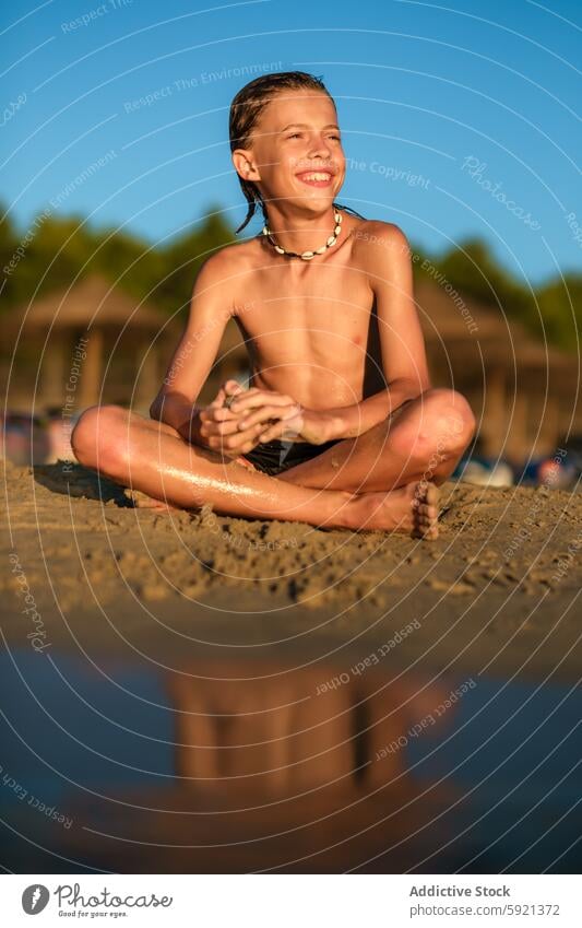 Shirtless boy looking away at beach smile sit sand vacation summer wet shirtless shell necklace legs crossed lifestyle water happy child reflection leisure