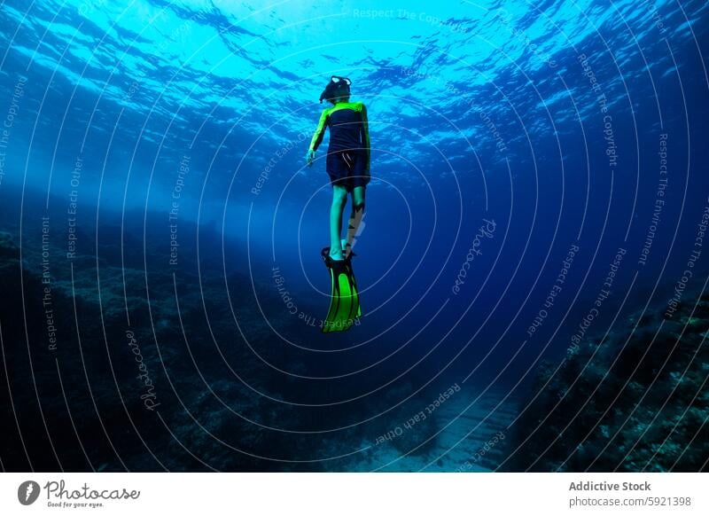 From below full body of unrecognizable active teen boy wearing yellow flippers snorkeling by coral reef in deep ocean with crystal clear waters at Menorca sea