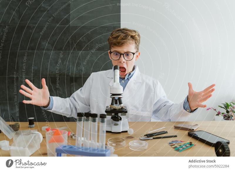 Surprised boy sitting at table with microscope and test tubes in school student surprise laboratory chemistry scientist flask science experiment research