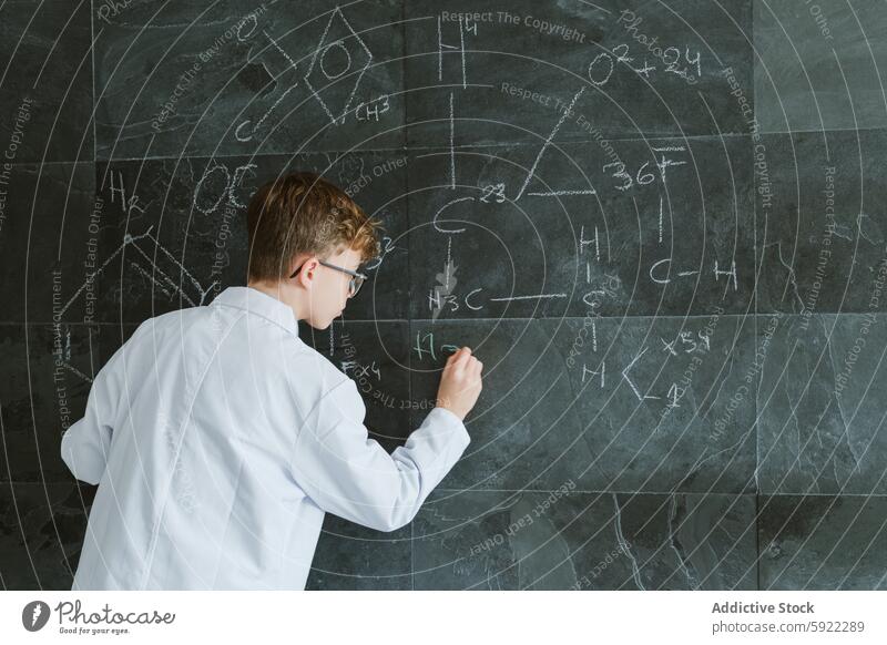 Focused schoolboy writing on chalkboard in classroom student science chemistry write formula blackboard education study kid uniform knowledge smart lesson