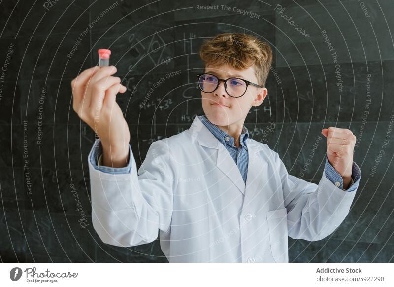 Boy showing test tubes while standing against blackboard in classroom boy school chemistry smart formula experiment chalkboard intelligent schoolkid lab child