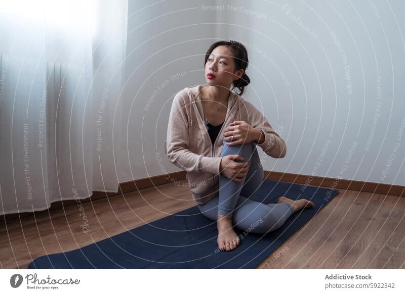 Young woman resting during yoga practice at home reflection athletic wear serene well-lit room sitting yoga mat meditation pause exercise mindfulness fitness