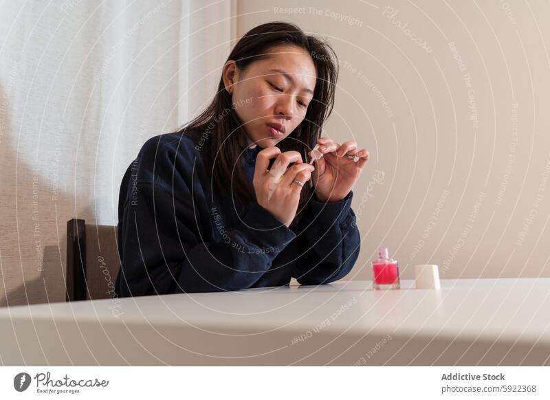 Woman applying nail polish at home woman self-care manicure pink focus delicate beauty grooming casual comfort relaxation table bottle concentrated routine diy