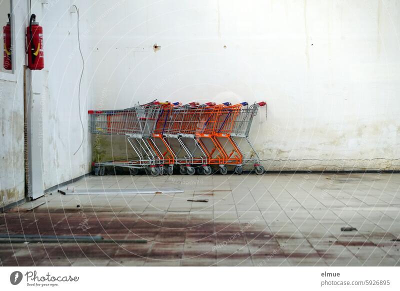 Old shopping carts and a fire extinguisher in an open, deserted large room of a closed supermarket Shopping Trolley Extinguisher Vacancy forsake sb./sth. Closed