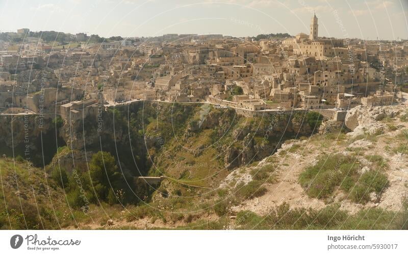 View of the gorge in front of the town and the old town of Matera (southern Italy) in the midday light. You can see ancient houses made of rock and caves carved into the rock. A church in the background.