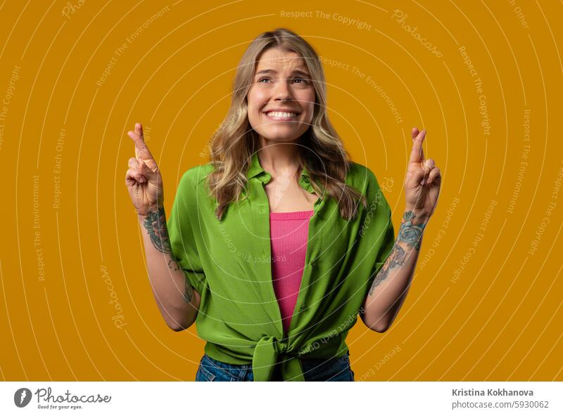 Stylish woman praying with crossed fingers, yellow background.Lady begs someone hope prayer hands belief faith god help religion young adult person please