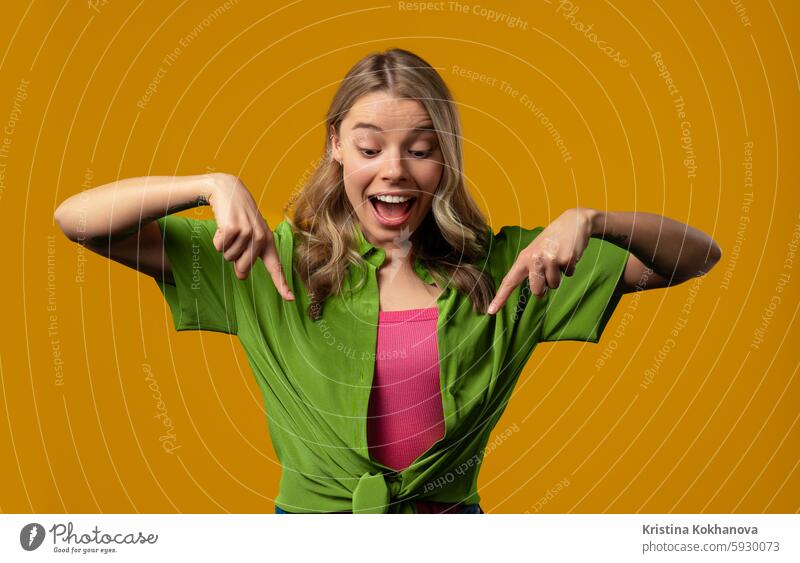 Blonde woman pointing down to advertising area.Yellow background.Click subscribe cheerful happiness happy recommend showing gesture hand model amazing attention