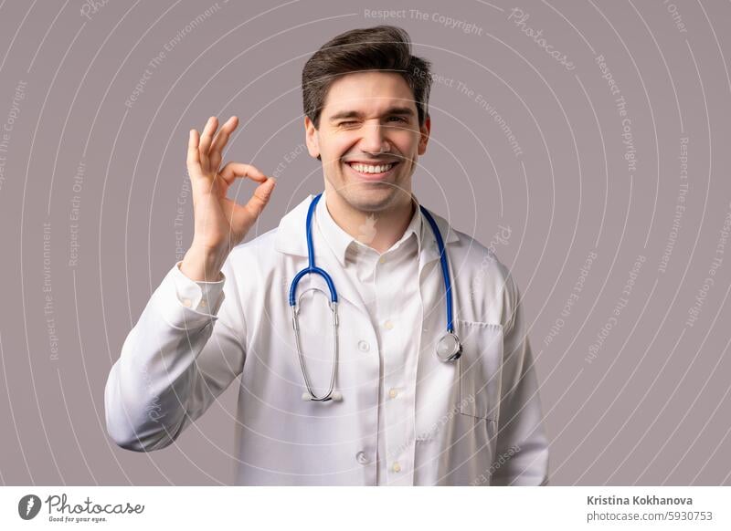 Doctor showing OK sign, white clinic studio background. Handsome doc man smiling achievement age agree agreement approval caucasian confident emotion finger