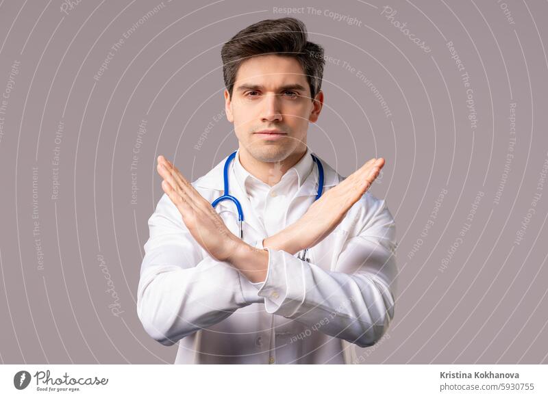 Serious doctor man showing NO crossing hands sign, rejecting gesture, stop palms medical person portrait serious adult background coat stethoscope young male