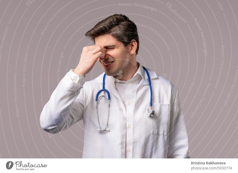 30s aged physician man in white medical coat form having headache, studio portrait. Guy putting hands on head, isolated on white background. Concept of problems, medicine, illness