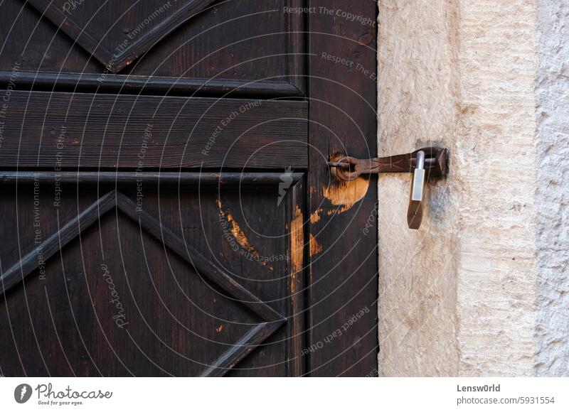 Weathered brown wooden door with a padlock antique building entrance close-up closed doorway gate house iron latch metal no people old old-fashioned protection