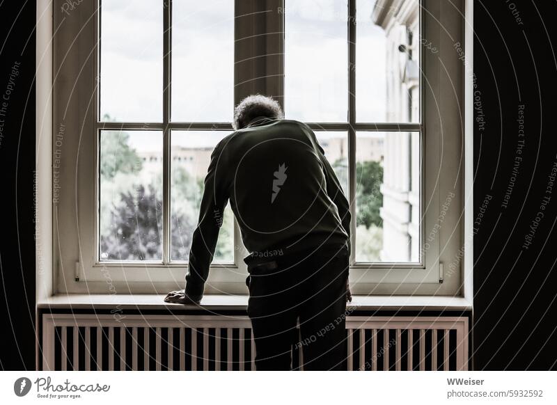 Tired and thoughtful, the old man leans on the window sill and looks out of the window tired Fatigue Exhaustion exhausted Old props ponder Meditative melancholy