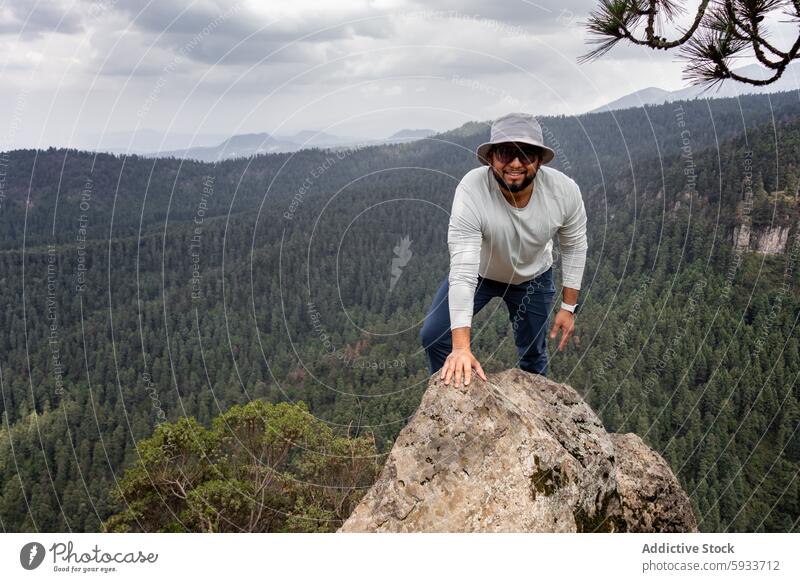 Man climbing rock in forest with mountain view man hiker bucket hat panoramic adventure nature outdoor male peak looking at camera wilderness tree landscape