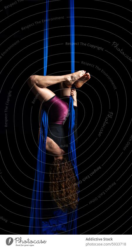 Back view of unrecognizable woman in aerial dance pose upside down modern flexibility strength blue silk performance artistic grace posture fabric suspended