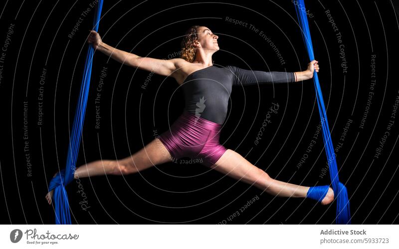 Female aerial dancer performing in blue silks against black woman flexibility strength dynamic split pose isolated black background performance fabric motion