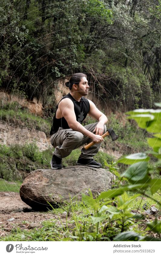 Man with an axe sitting on a rock in a lush forest man nature greenery rugged thoughtful serene outdoor adventure exploring foliage environment peaceful