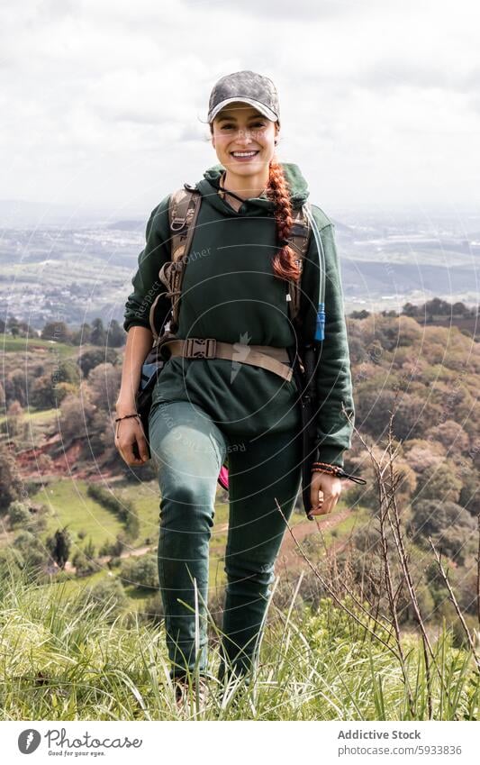 Young woman hiking with a scenic valley background nature outdoor backpack smile landscape adventure travel leisure activity green grass sky caucasian female