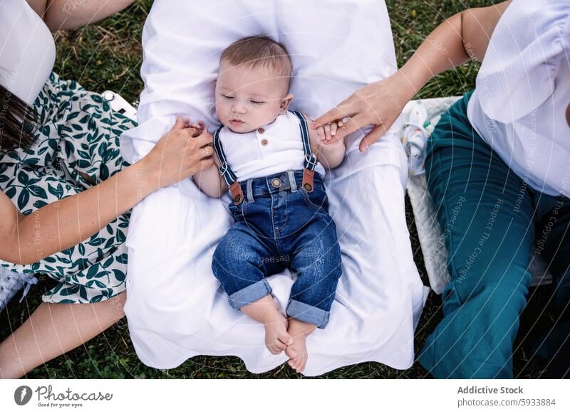 Baby holding hands with lesbian couple during outdoor relaxation baby boy lgbt woman infant child colombian family parent mother father outdoors blanket love