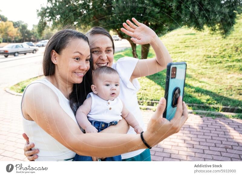 Lesbian couple taking a selfie with their baby son in park family lesbian smartphone joy happiness love afternoon outdoor sunny casual diverse woman partner